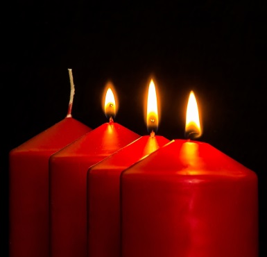 Drei rote Kerzen brennen zu Advent in einer Reihe von vier Kerzen.
