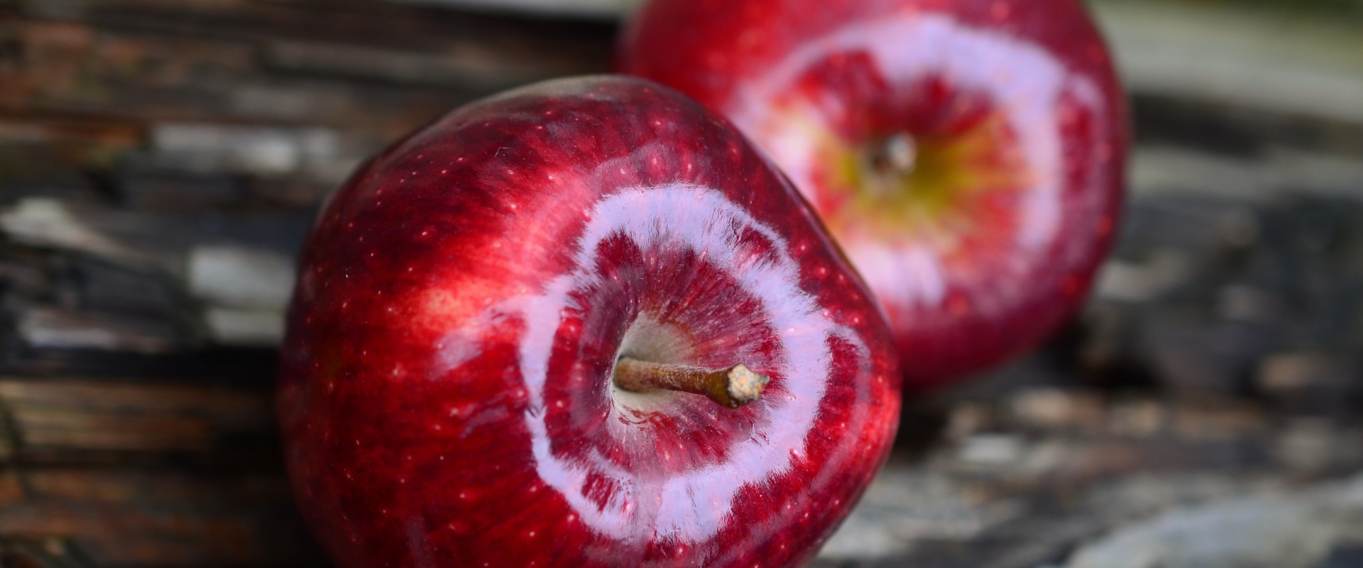 Zwei schön polierte rote Weihnachtsäpfel liegen auf einer Holzplatte.