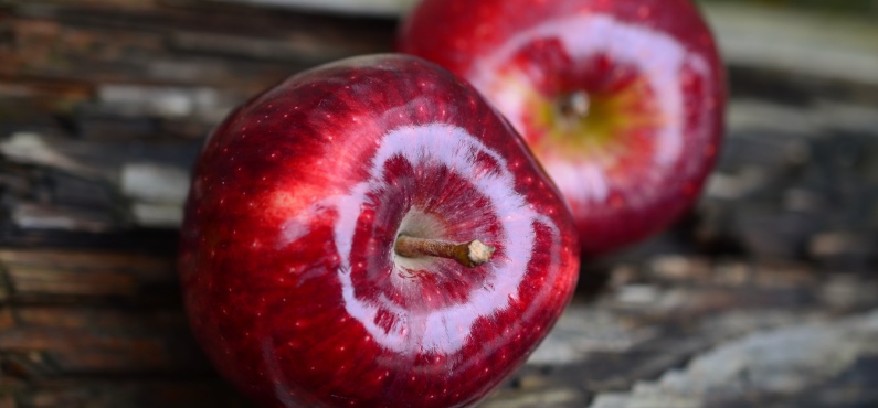 Zwei schön polierte rote Weihnachtsäpfel liegen auf einer Holzplatte.