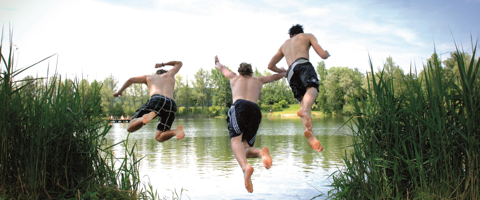 Drei Männer die in den Peracher Badesee in Bayern hüpfen im Rahmenprogramm des Altöttinger Forums.