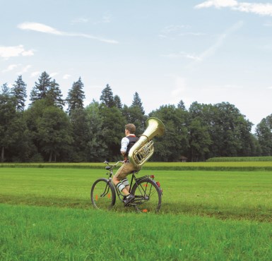 Ein Musiker, der mit seiner Tuba auf dem Rücken mit dem Fahrrad fährt im Rahmenprogramm des Altöttinger Forums.