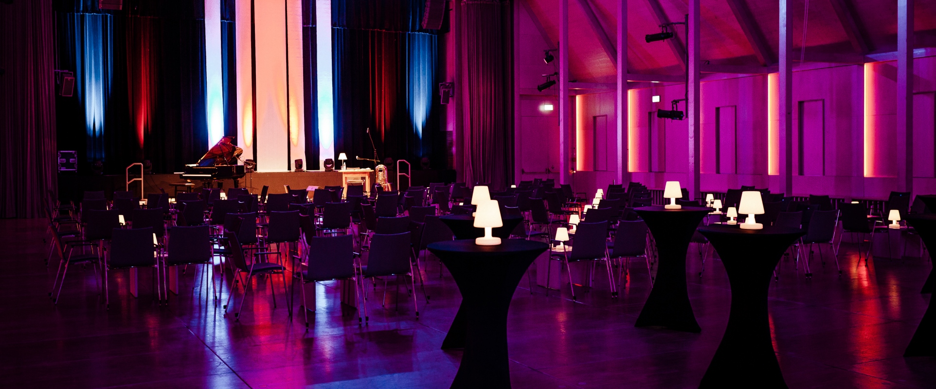 Der Raiffeisen Saal mit Beistelltischen und lila Beleuchtung bei dem Auftritt von Andreas Hofmeier im Forum Altötting.