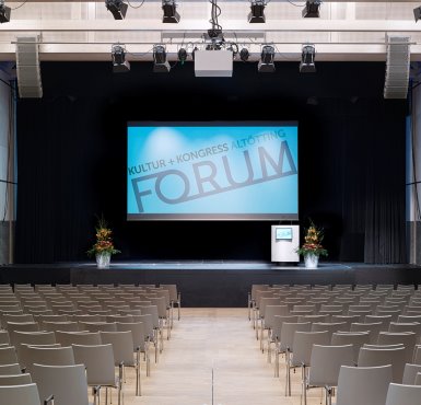 Der Raiffeisen-Saal mit Reihenbestuhlung, Leinwand und Rednerpult auf der Bühne im Forum Altötting.