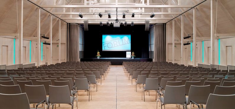 Der Raiffeisen-Saal mit Reihenbestuhlung, Leinwand und Rednerpult auf der Bühne im Forum Altötting.