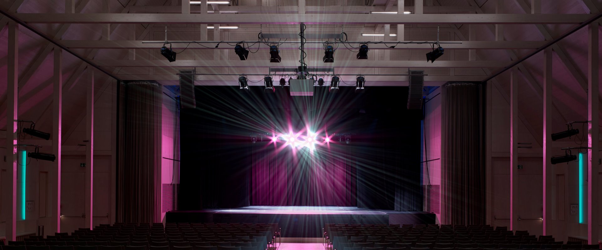 Der Raiffeisen-Saal mit Reihenbestuhlung und rosa Beleuchtung auf der Bühne im Forum Altötting.
