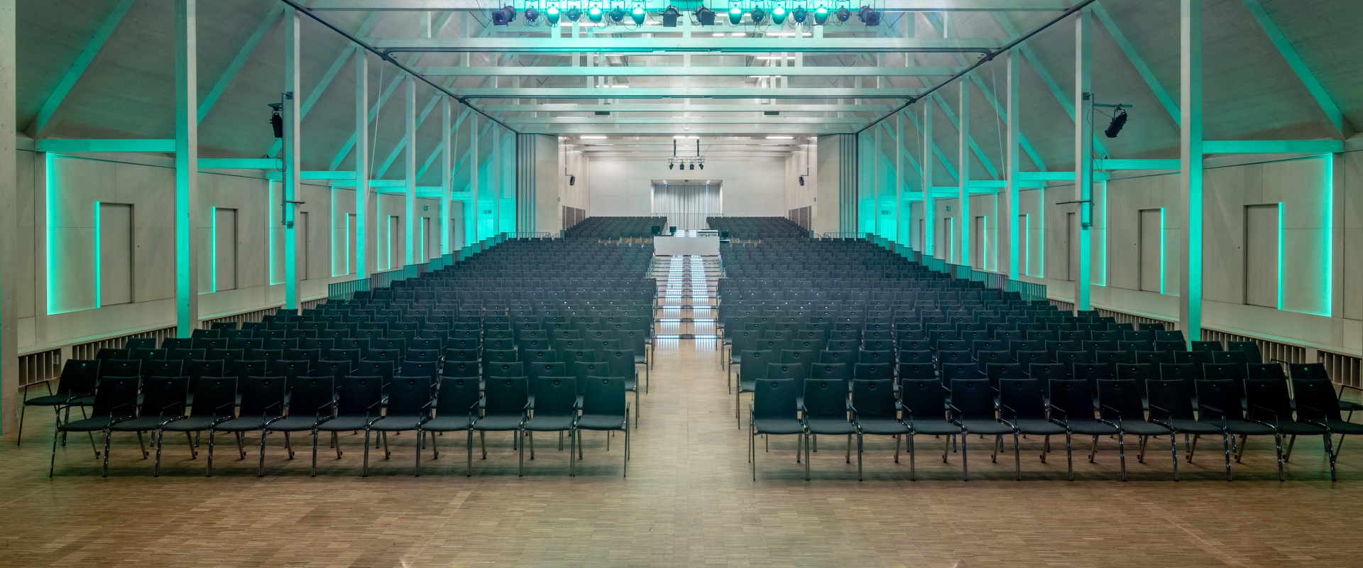 Die Reihenbestuhlung im Raiffeisen-Saal gestuft auf den Stufenpodesten mit türkiser Beleuchtung im Forum Altötting.