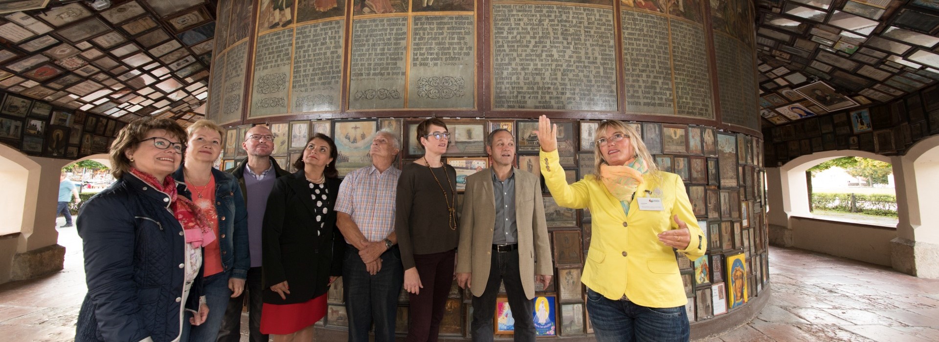 Eine Stadtführungsgruppe steht im Umgang der Gnadenkapelle in Altötting während die Stadtführerin der Gruppe die Votivtafeln erläutert. 